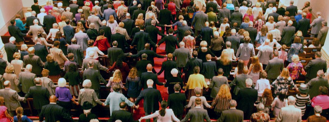St James service A diverse group of people, holding hands, stands together in rows, possibly in a religious or community gathering, inside a large hall.