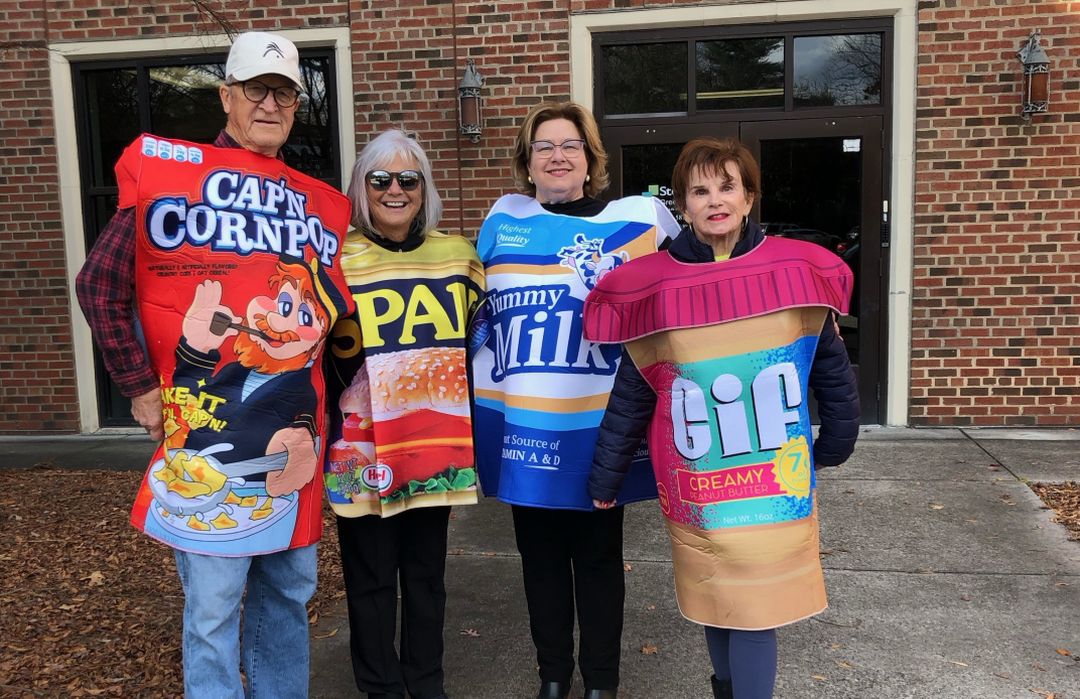 MAKE A DIFF pic1 Four people in food-themed costumes, including cereal, peanut butter, and milk, standing outside a building with a brick facade.